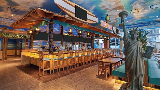 A bar area with a wooden bar counter, seating, and a statue of the Statue of Liberty. - Margaritaville Resort Times Square (New York)
