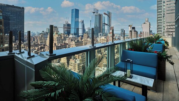 A rooftop terrace with a city skyline view, blue seating, and potted plants. - Margaritaville Resort Times Square (New York)