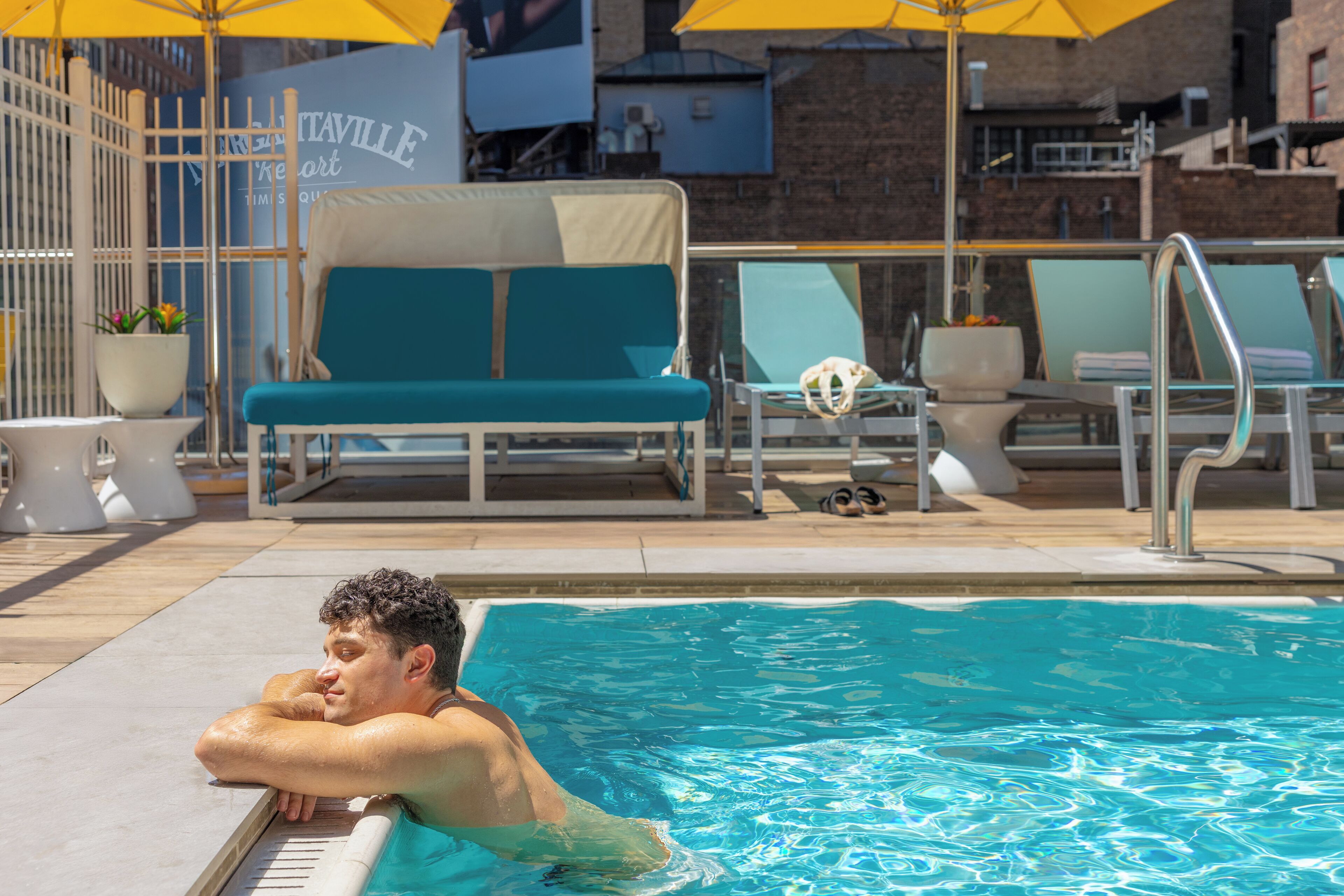 A poolside area with lounge chairs, a covered seating area, and a sign for 'Tavaville Resort'.