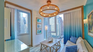 A modern living room with a glass coffee table, a beige sofa with patterned cushions, and a large window offering a city view. - Margaritaville Resort Times Square (New York)