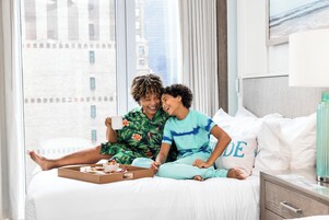 Una habitación de hotel con cama, mesita de noche y ventana con vista a la ciudad.