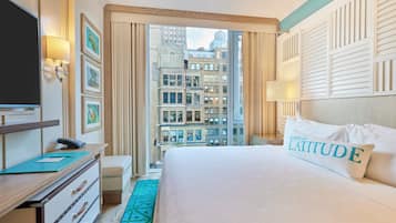 A hotel room with a large bed, a desk with a telephone, a television, and a view of the cityscape through the window.