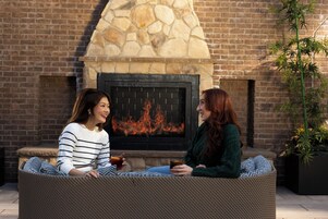 Two people sitting on wicker furniture in front of a stone fireplace with a fire.