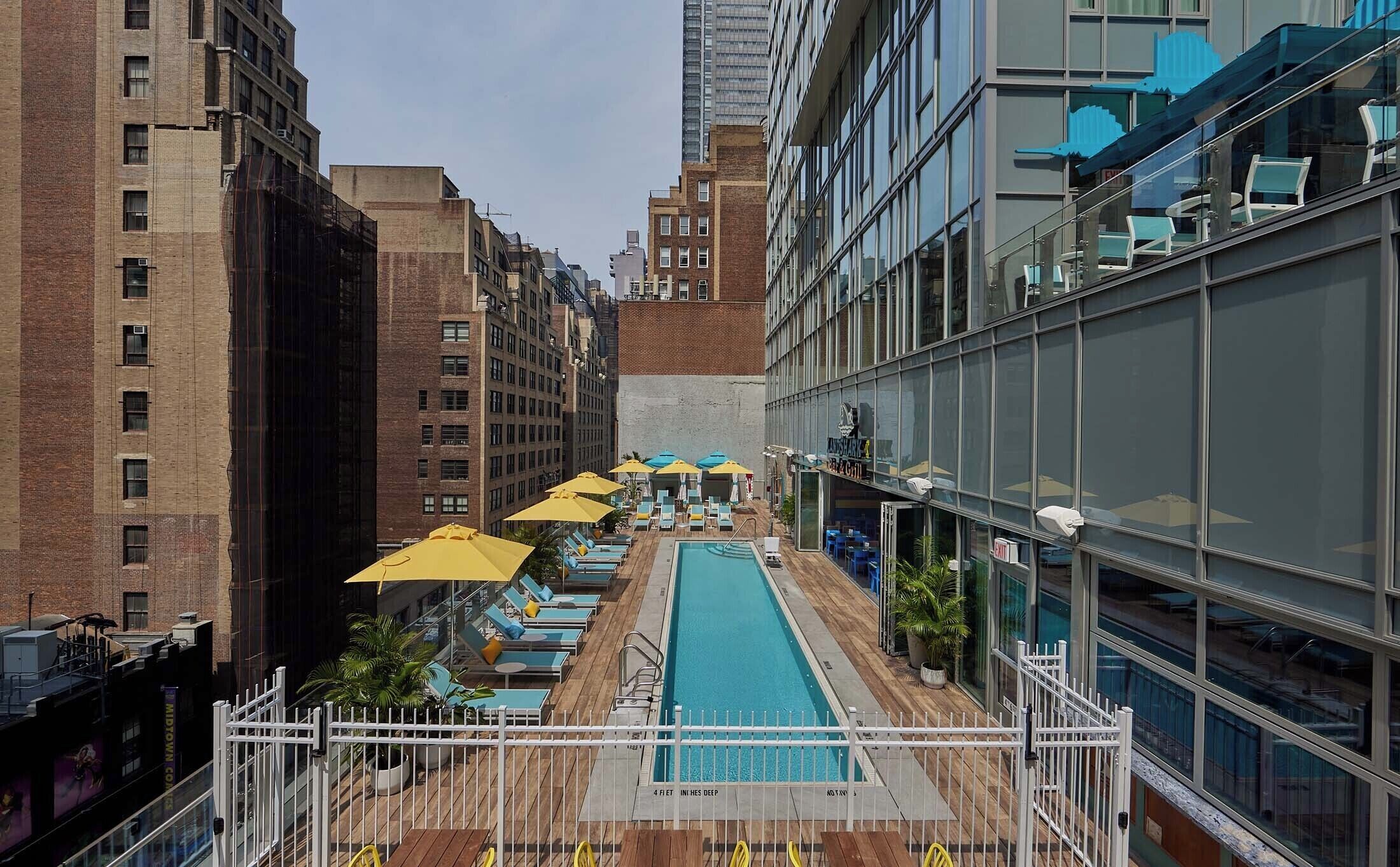 A rooftop pool with sun loungers and umbrellas, surrounded by high-rise buildings.