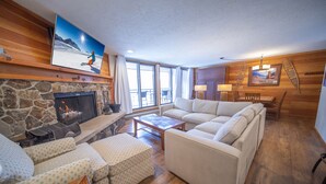 A cozy living room with a stone fireplace, a large sofa, a coffee table, and a television mounted on the wall. - Montezuma 1770 (Keystone)
