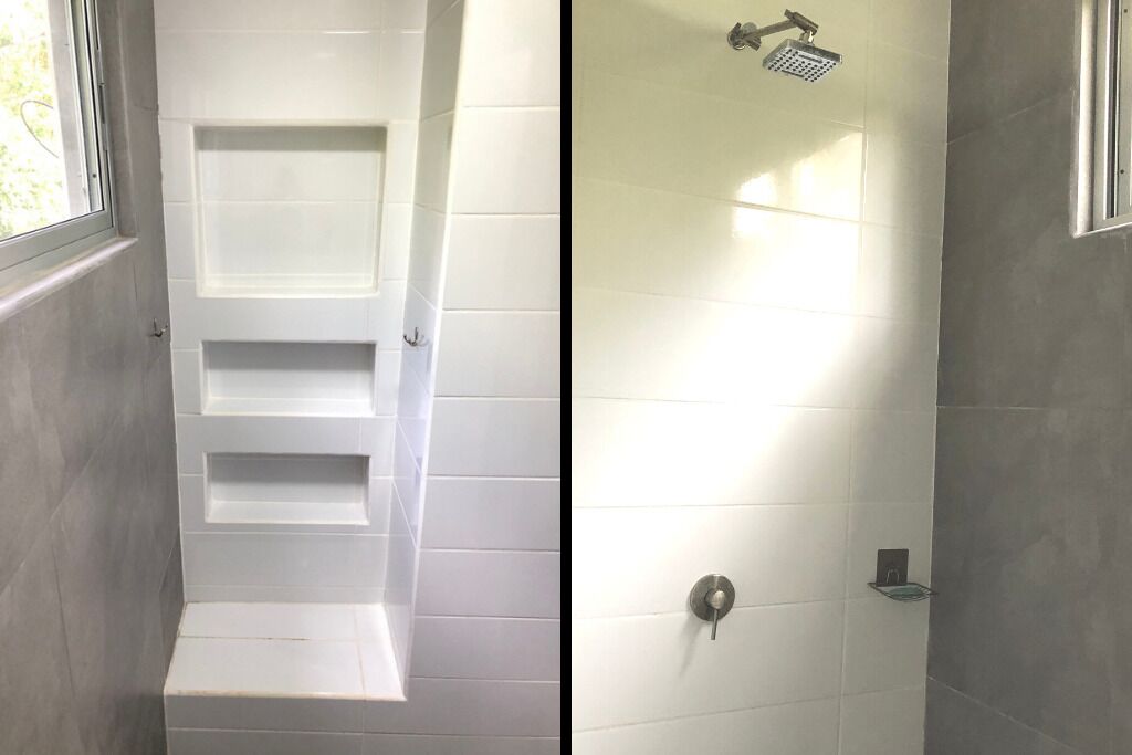 Ein Badezimmer mit einer weißen Duschkabine, einer Glasduschtür und einer weißen Badewanne mit integrierten Ablagen.