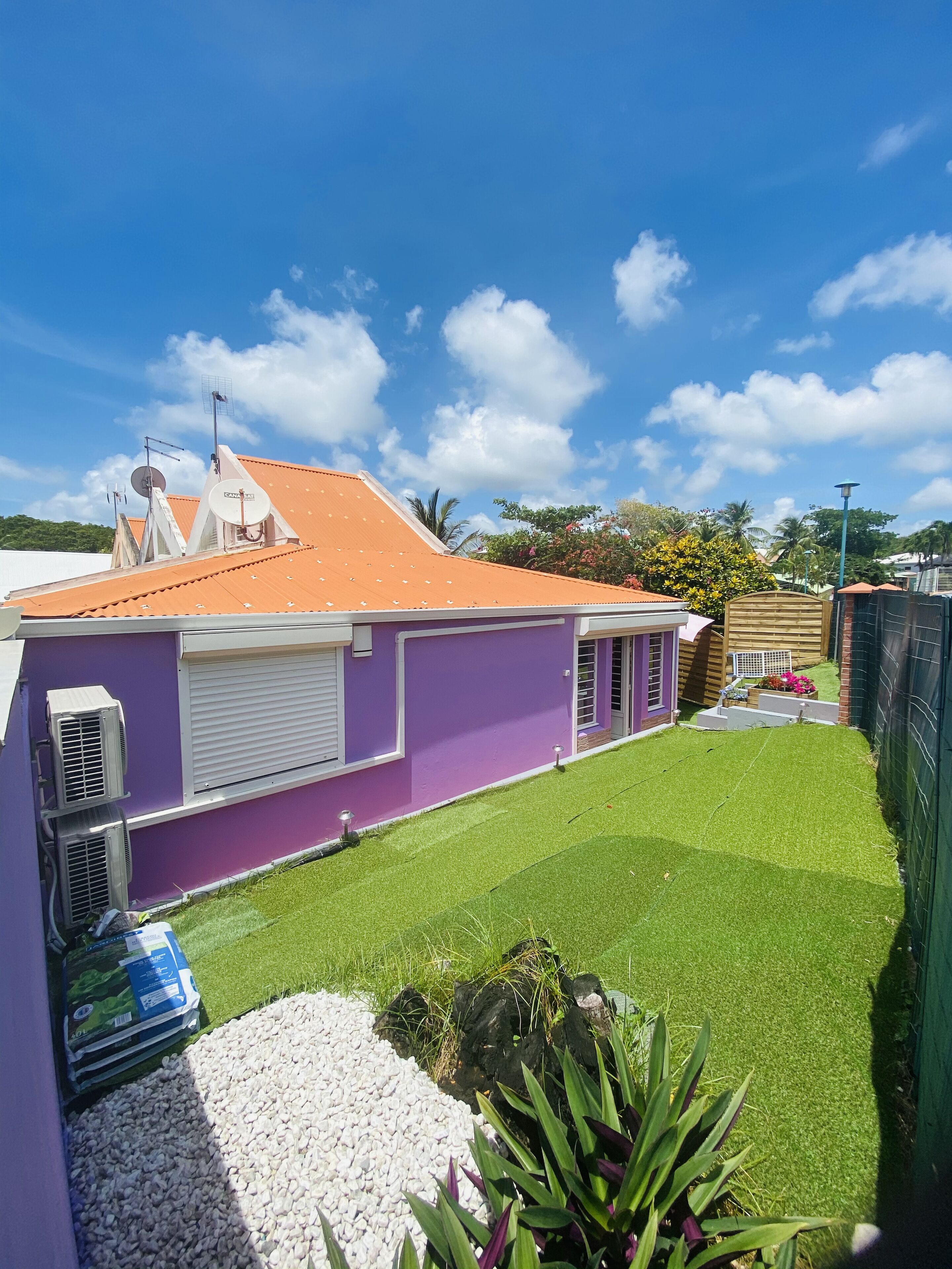 A purple building with a sloped orange roof, air conditioning units, and a well-maintained lawn.