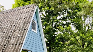 Une maison bleue avec un toit en pente, une porte d’entrée et un petit porche avec des marches menant à la porte.
