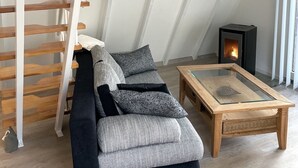 Un salon de style industriel, avec un escalier en bois, un canapé, une table basse en verre et un poêle à bois.