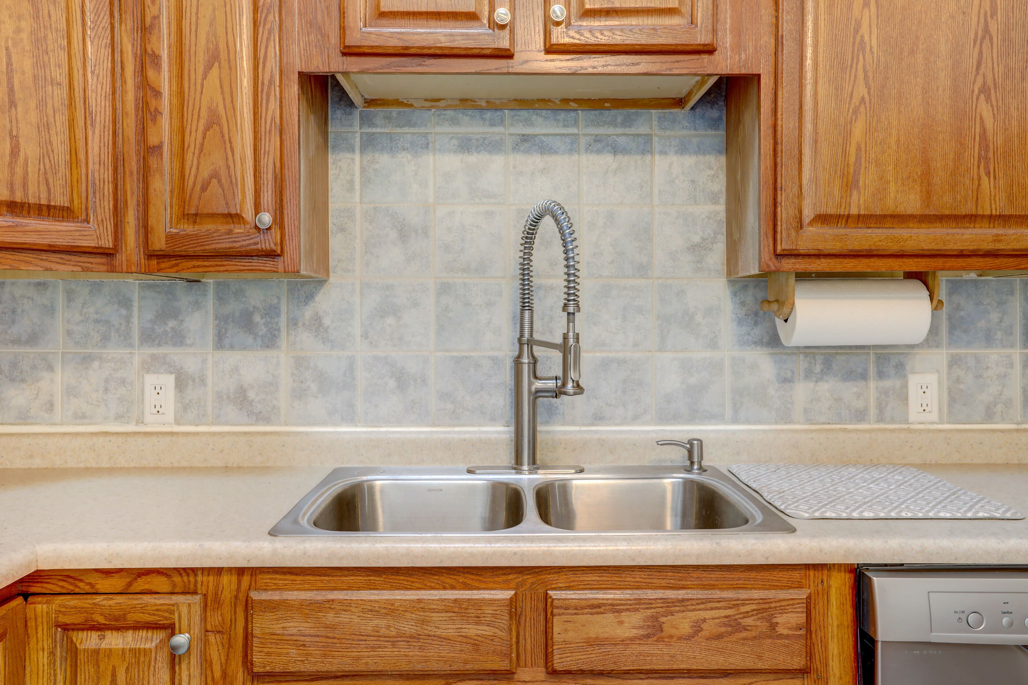 Cozinha com armários de madeira, pia de aço inoxidável e backsplash revestido de azulejos.