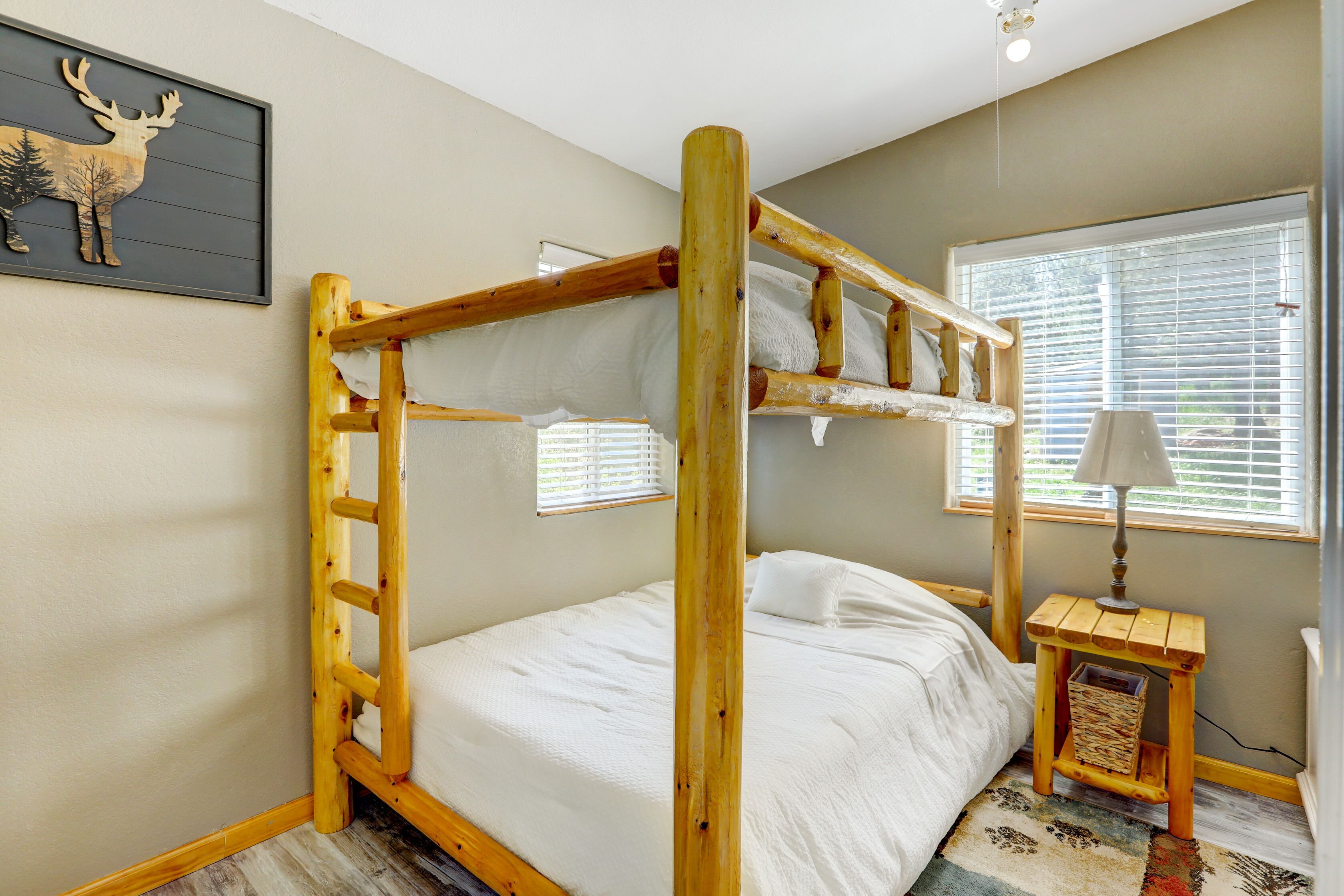 A bunk bed with a wooden ladder, a small bedside table with a lamp, and a framed deer picture on the wall.