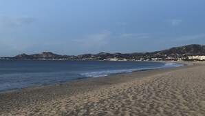 Ein sandiger Strand mit blauem Himmel und sanften Hügeln in der Ferne.