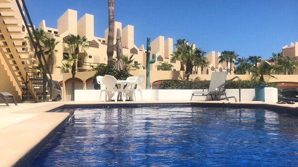 Ein Swimmingpool mit klarem, blauem Wasser, umgeben von Palmen und weißen Liegestühlen.