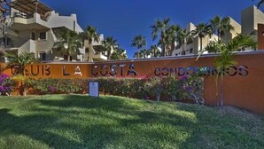 Schild für 'Club La Costa Condominiums' mit gepflegtem Rasen und Palmen.