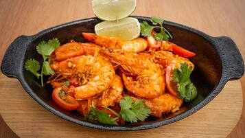 Una sartén con camarones cocidos, tomates y cilantro, adornada con rodajas de lima.