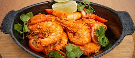 Una sartén con camarones cocidos, tomates y cilantro, adornada con rodajas de lima.