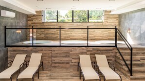 A spa area with a wooden floor, two sun loungers, a glass railing, and a view of greenery through large windows. - Solar Pedra da Ilha (Penha)