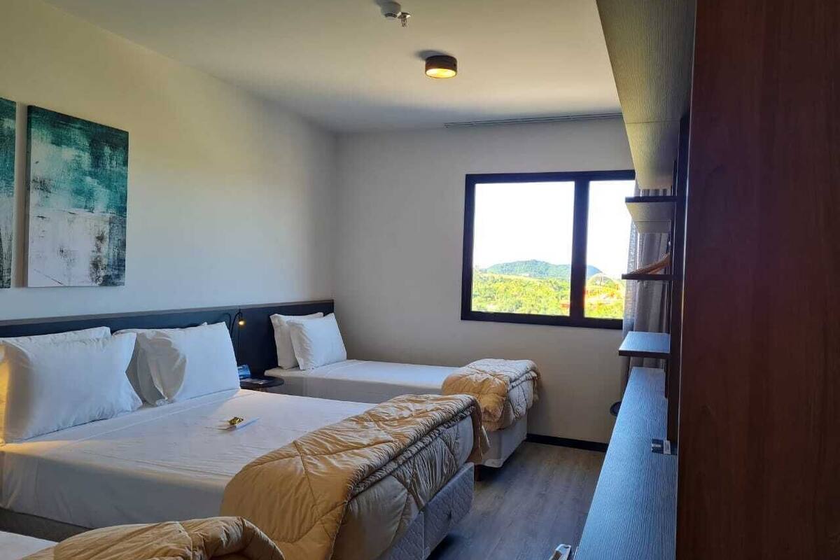 A hotel room with two beds, a large window with a view of the outdoors, and a ceiling light fixture.
