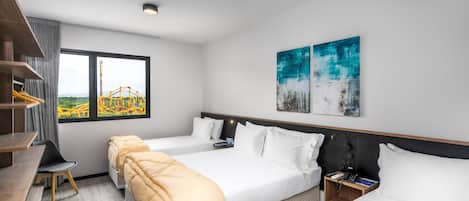 A modern hotel room with two beds, a desk, and a chair. There is a window with a view of a roller coaster.