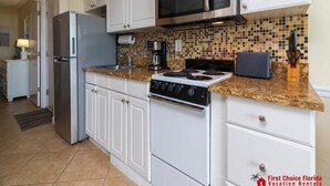 A kitchen with white cabinets, a stainless steel refrigerator, a microwave, a stove, and a coffee maker. - Spectacular Oceanfront Views ~ Olympic Sized Heated Oceanfront Pool (Saint Augustine)