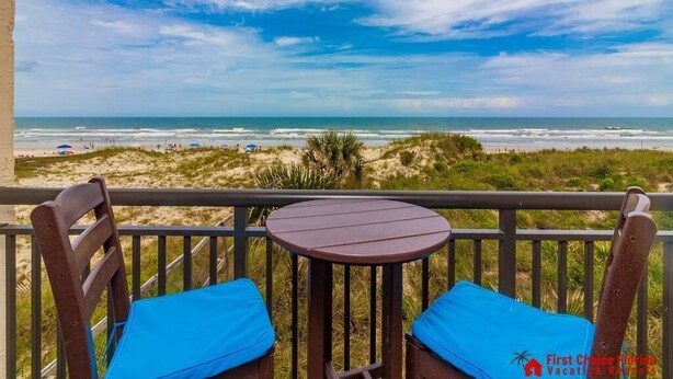 A balcony with a table and two chairs, overlooking a beach with dunes and the ocean. - Spectacular Oceanfront Views ~ Olympic Sized Heated Oceanfront Pool (Saint Augustine)