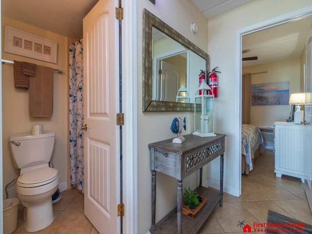 Een badkamer met toilet, douchegordijn en een wastafel met spiegel en een klein tafeltje.