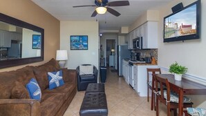 A living room with a brown sofa, a black ottoman, a ceiling fan, and a dining area with a wooden table and chairs. - Spectacular Oceanfront Views ~ Olympic Sized Heated Oceanfront Pool (Saint Augustine)