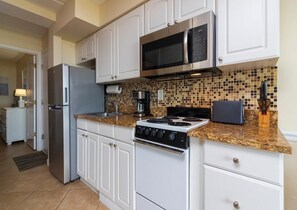 A kitchen with white cabinets, a stainless steel refrigerator, a microwave, a stove, and a coffee maker.