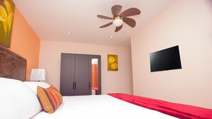 Una habitación de hotel con cama, ventilador de techo, televisor, armario y un cuadro en la pared.