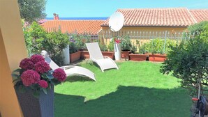 Un patio con dos sillones blancos, un jardín pequeño con césped artificial y una antena parabólica.