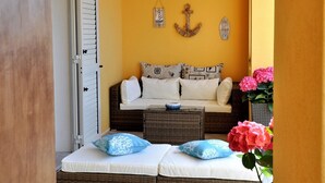 Una habitación acogedora con un sofá de mimbre, dos almohadas blancas, una lámpara colgante y un adorno de ancla en la pared.