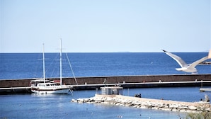 Un puerto con un barco amarrado en el muelle, una gaviota volando y agua azul tranquila.