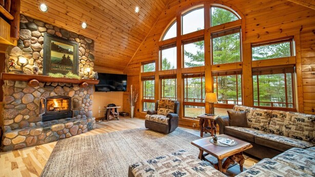 A cozy cabin interior with a stone fireplace, large windows, and wooden furnishings. - Spacious Lakefront Lodge, Kayaks/Canoes Included! Pet Friendly! (Tomahawk)