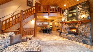A cozy cabin interior with a stone fireplace, wooden staircase, and a dining area. - Spacious Lakefront Lodge, Kayaks/Canoes Included! Pet Friendly! (Tomahawk)