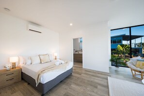 A modern bedroom with a large bed, bedside lamps, and a view of the outdoors. - Airlie Bay View (Airlie Beach)