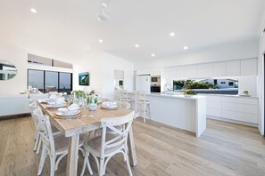 Eine moderne Küche mit weißen Schränken, einem Holzespeise Tisch für sechs Personen und einer großen Kochinsel mit Spüle.