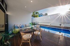 A modern outdoor living area with a pool, wooden deck, and seating. - Airlie Bay View (Airlie Beach)