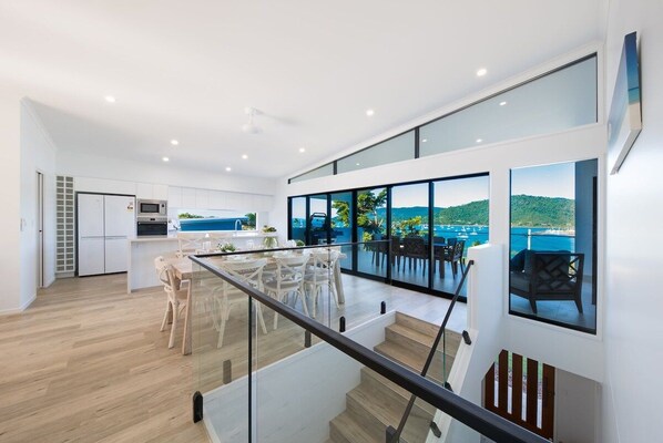 A modern kitchen with a dining area, large windows with a view, and a staircase leading to an upper level. - Airlie Bay View (Airlie Beach)