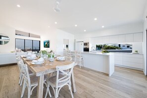A modern kitchen with white cabinetry, a central island, and a dining area with a wooden table and white chairs. - Airlie Bay View (Airlie Beach)