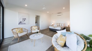 A modern living room with a sofa, chairs, a coffee table, and a bed in the background. - Airlie Bay View (Airlie Beach)