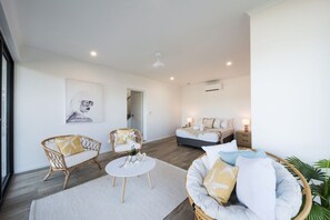 A modern living room with a sofa, chairs, a coffee table, and a bed in the background. - Airlie Bay View (Airlie Beach)