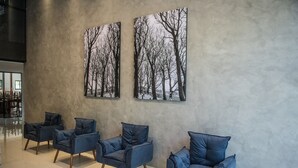 Un interior moderno con cuatro sillones azul oscuro alineados frente a una pared texturizada, y dos cuadros grandes enmarcados que muestran un paisaje de bosque nevado.
