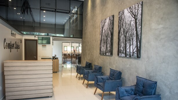 Zona de recepción de hotel con diseño moderno, que incluye mostrador de recepción, área de descanso con sillas y obras de arte en las paredes.