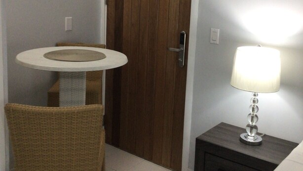 Un bagno piccolo con una porta in legno, un lavandino rotondo, una sedia in vimini e un comodino con una lampada.