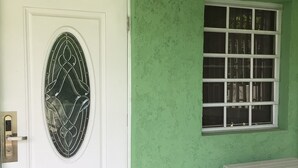 Una stanza con una porta bianca con un pannello di vetro decorativo, una finestra a più riquadri e una sedia in vimini nero.