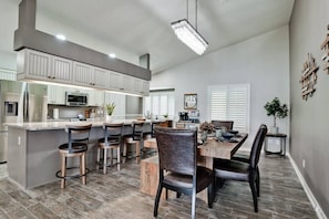 A modern kitchen with a central island, bar stools, and a dining table with chairs.