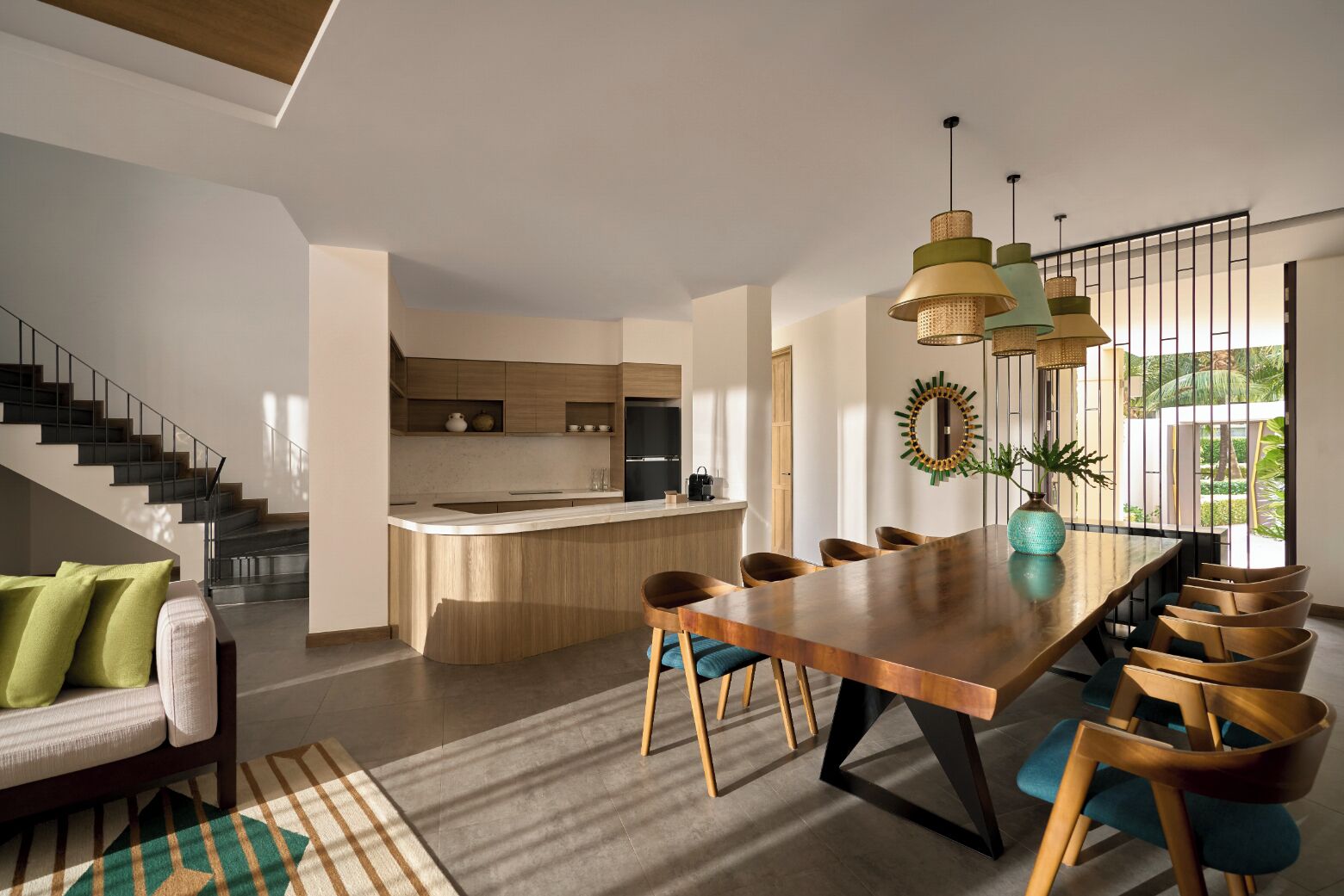 A modern kitchen with a central island, a dining area with a wooden table and chairs, and a staircase leading to an upper level.