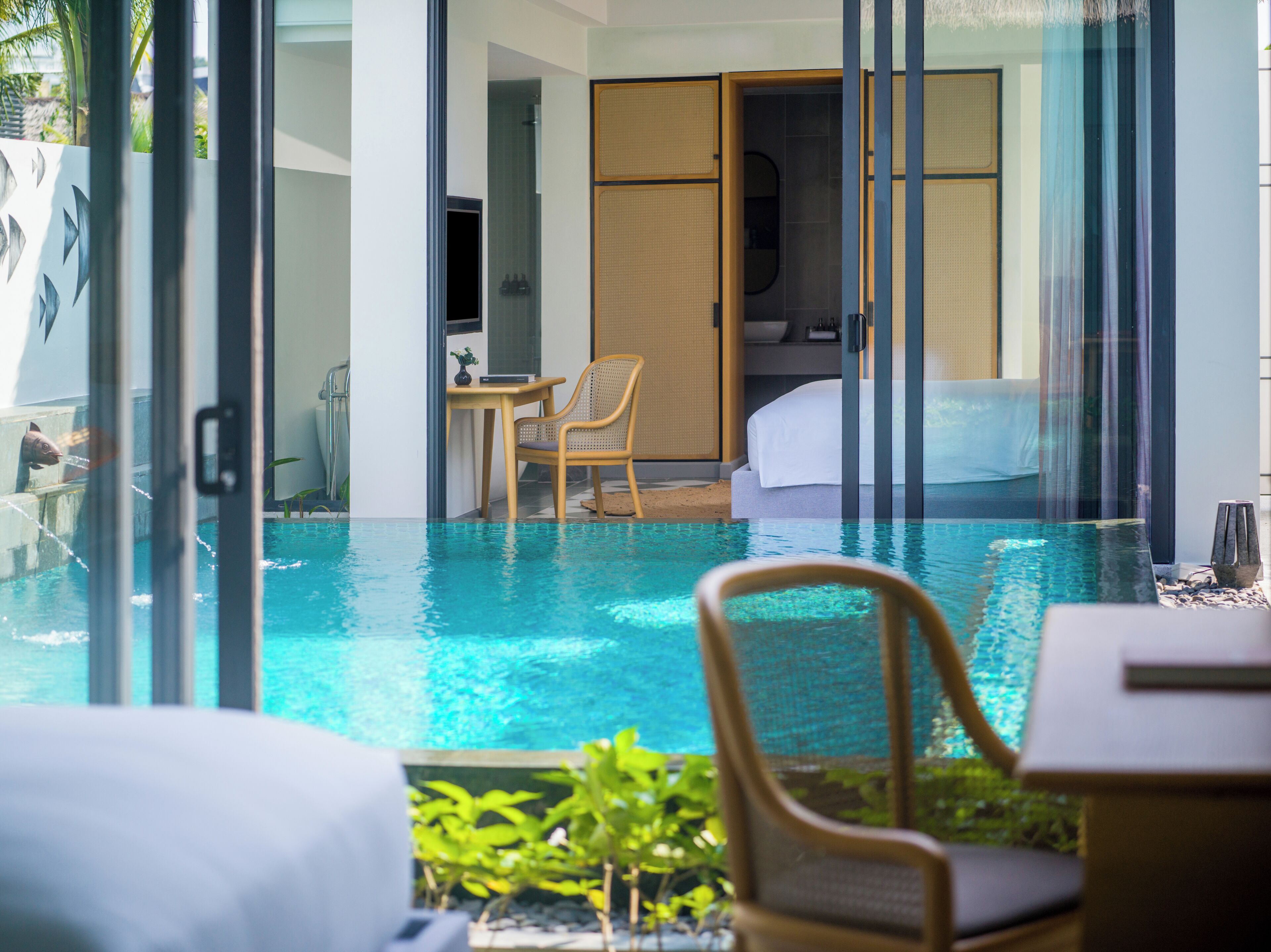 Una habitación de hotel moderna con piscina en cristal, cama, una mesita y una silla.