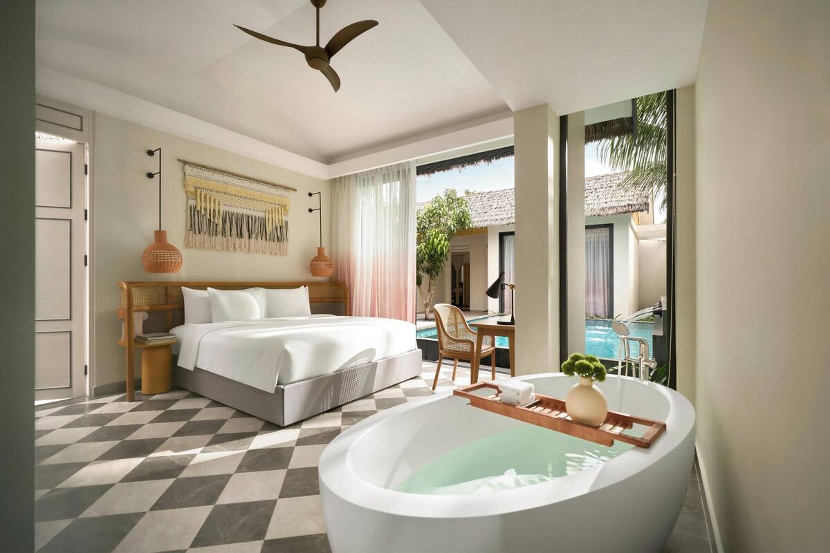 A hotel room with a large bed, a bathtub, a dining area, and a view of a pool.