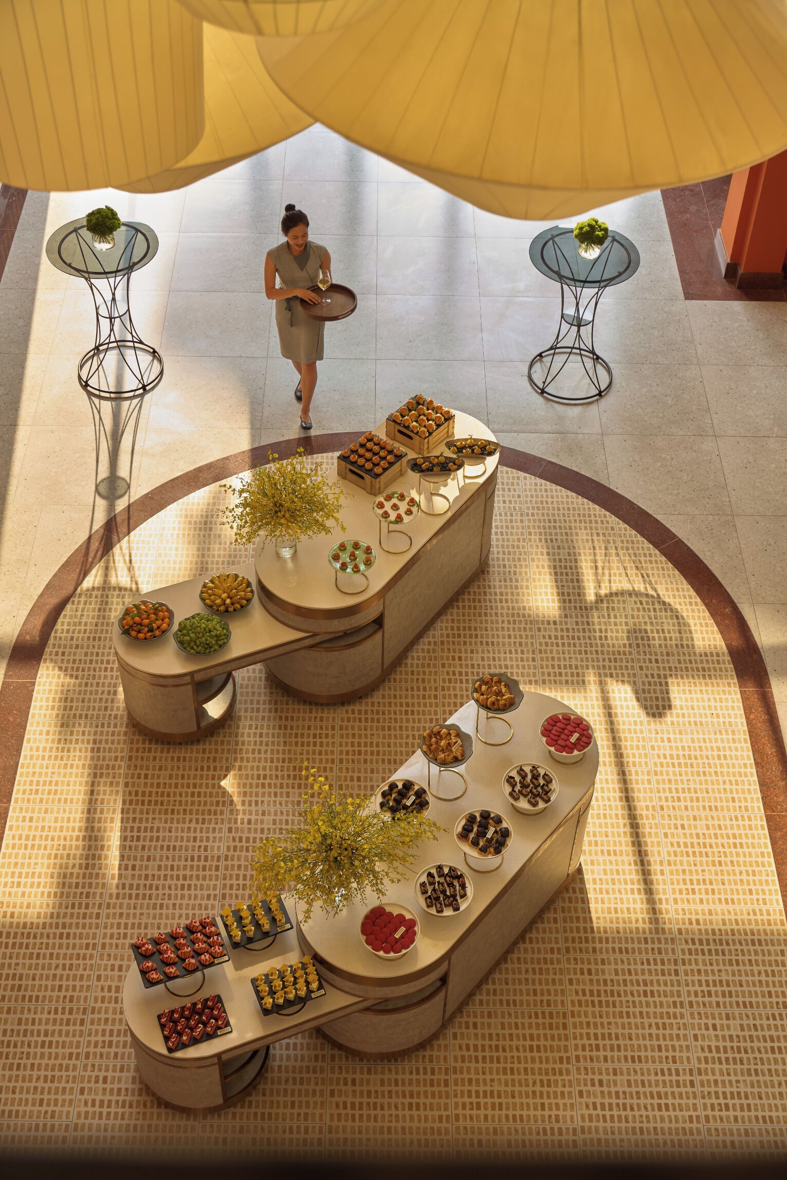 Un amplio atrium con una mesa de buffet central que ofrece diversas opciones de comida y una persona atendiendo.